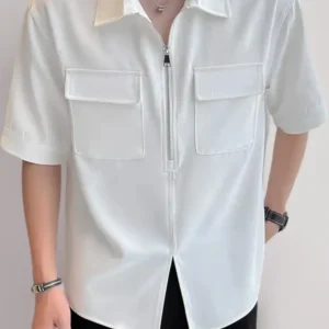 Front view of a man wearing a crisp white short-sleeved utility shirt featuring a central silver zipper, two symmetrical chest flap pockets, and a classic pointed collar.