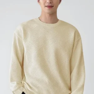 Man wearing a cream textured knit sweater with black pants in a minimal studio background.