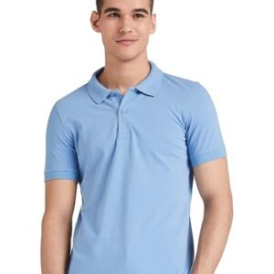 A young man with short dark hair wearing a light blue polo shirt, standing against a plain light background with one hand in his pocket.