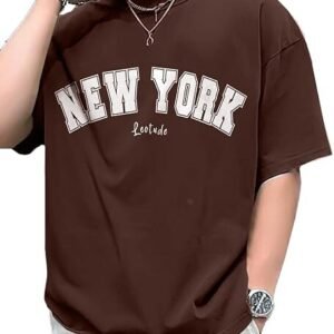 A person wearing an oversized chocolate brown t-shirt featuring "NEW YORK" in large cream-colored collegiate block letters with a white outline, accessorized with silver jewelry.