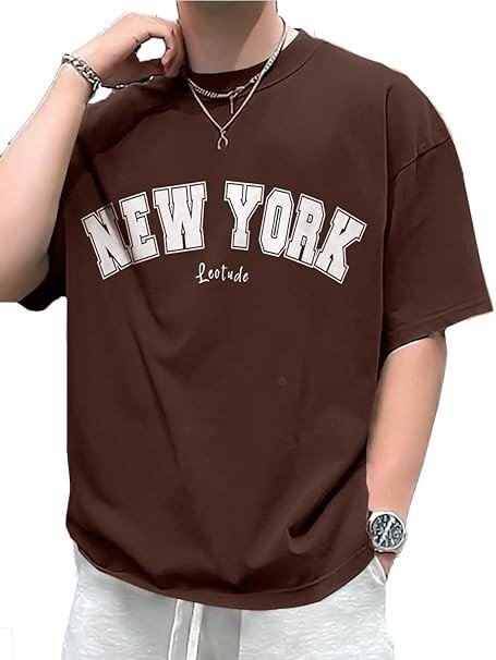A person wearing an oversized chocolate brown t-shirt featuring "NEW YORK" in large cream-colored collegiate block letters with a white outline, accessorized with silver jewelry.